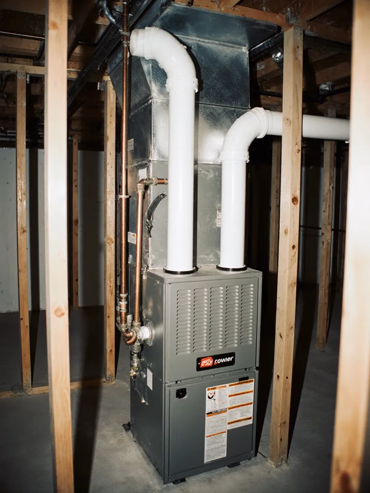 New high-efficiency furnace in a basement with white PVC venting